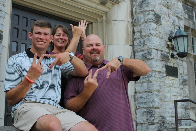 Jack Wilson sits outside the entrance to Hutcheson Hall with his parents Kelli and Raymond Wilson as they gesture VT hands.