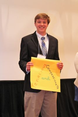 Ethan Wagoner holds up sign with the words "tenacious and compassionate" on it