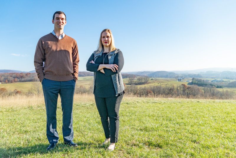 Patrick Kayser and Jennifer Friedel stand at the top of a hill with farmland in the background.