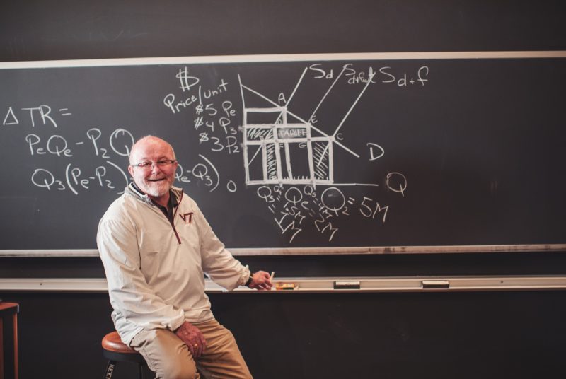 Professor Mike Ellerbrock sits in front of chalkboard after drawing economic diagram.